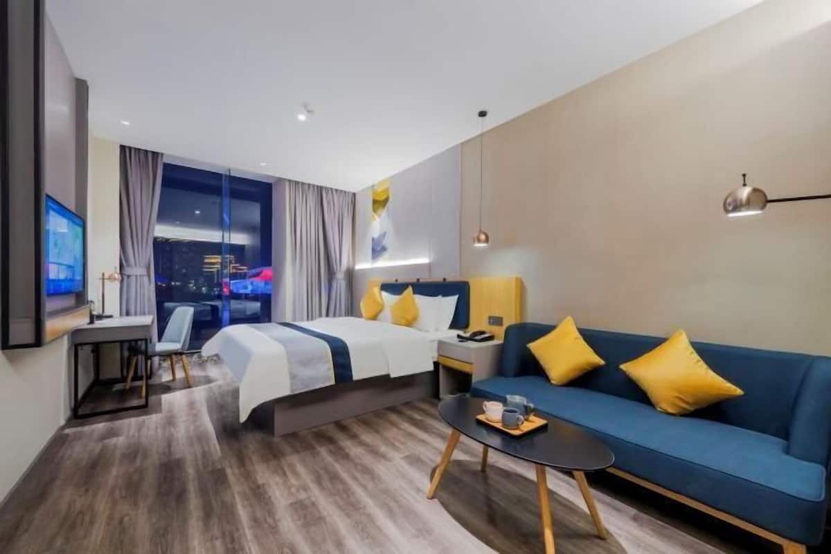 A modern hotel room with a bed, a sofa, a desk, and a view of the city at night.