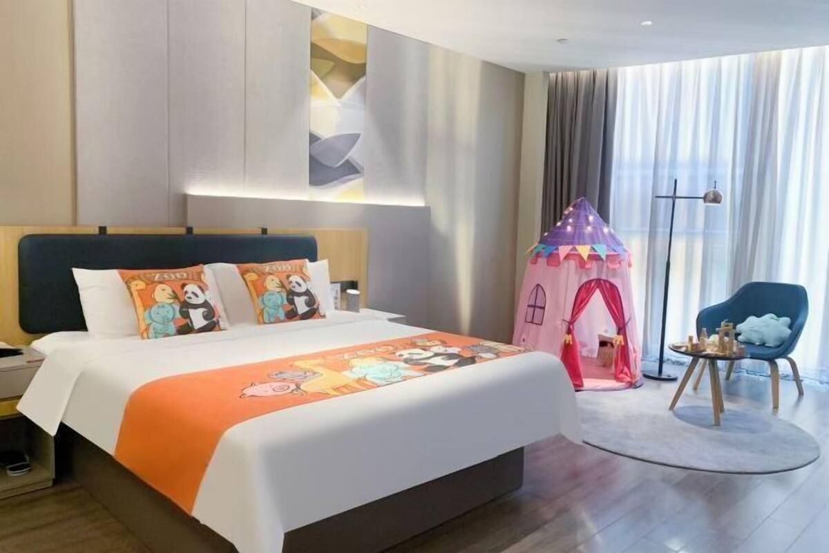 A hotel room with a large bed, a pink play tent, a blue armchair, and a modern lamp.