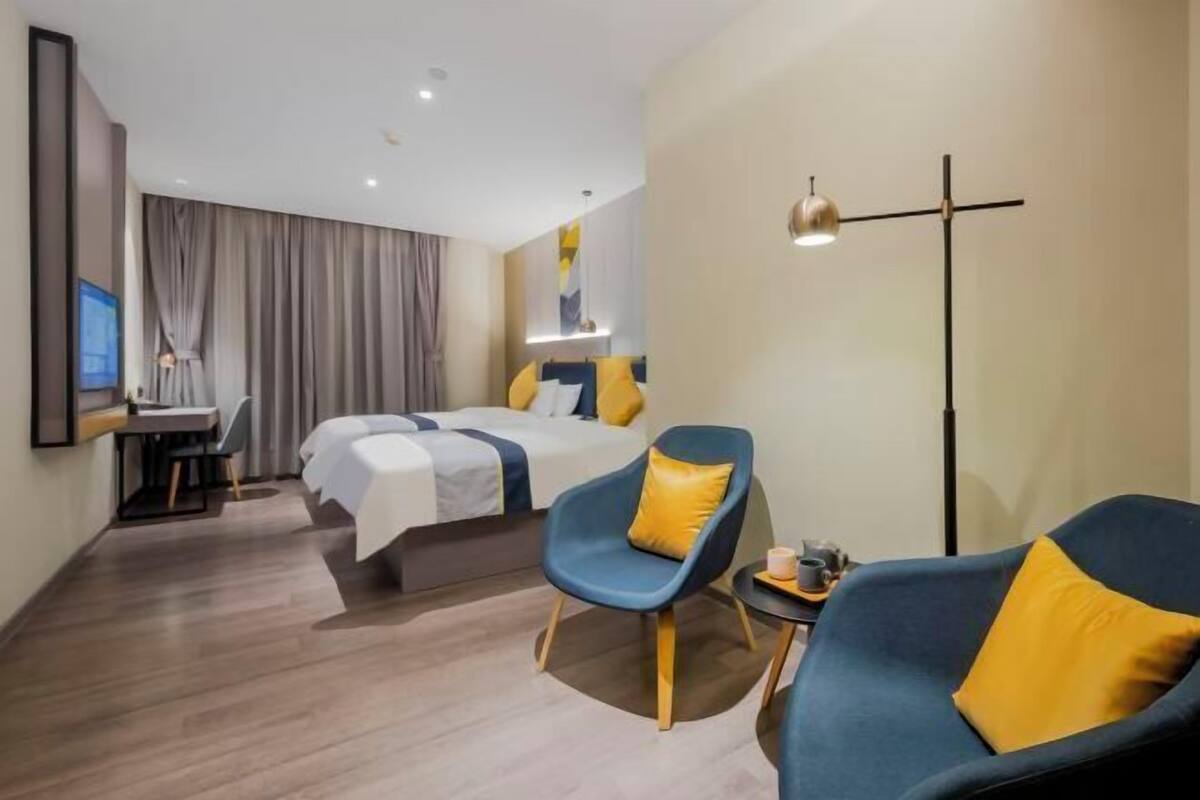 A hotel room with two beds, a desk, a chair, and a floor lamp.