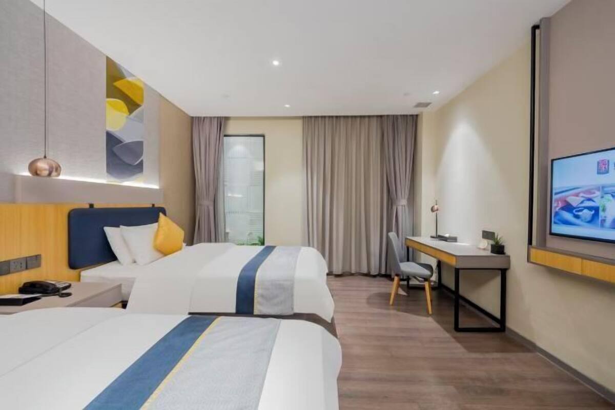 A hotel room with two beds, a desk, a chair, a TV, and a window with curtains.