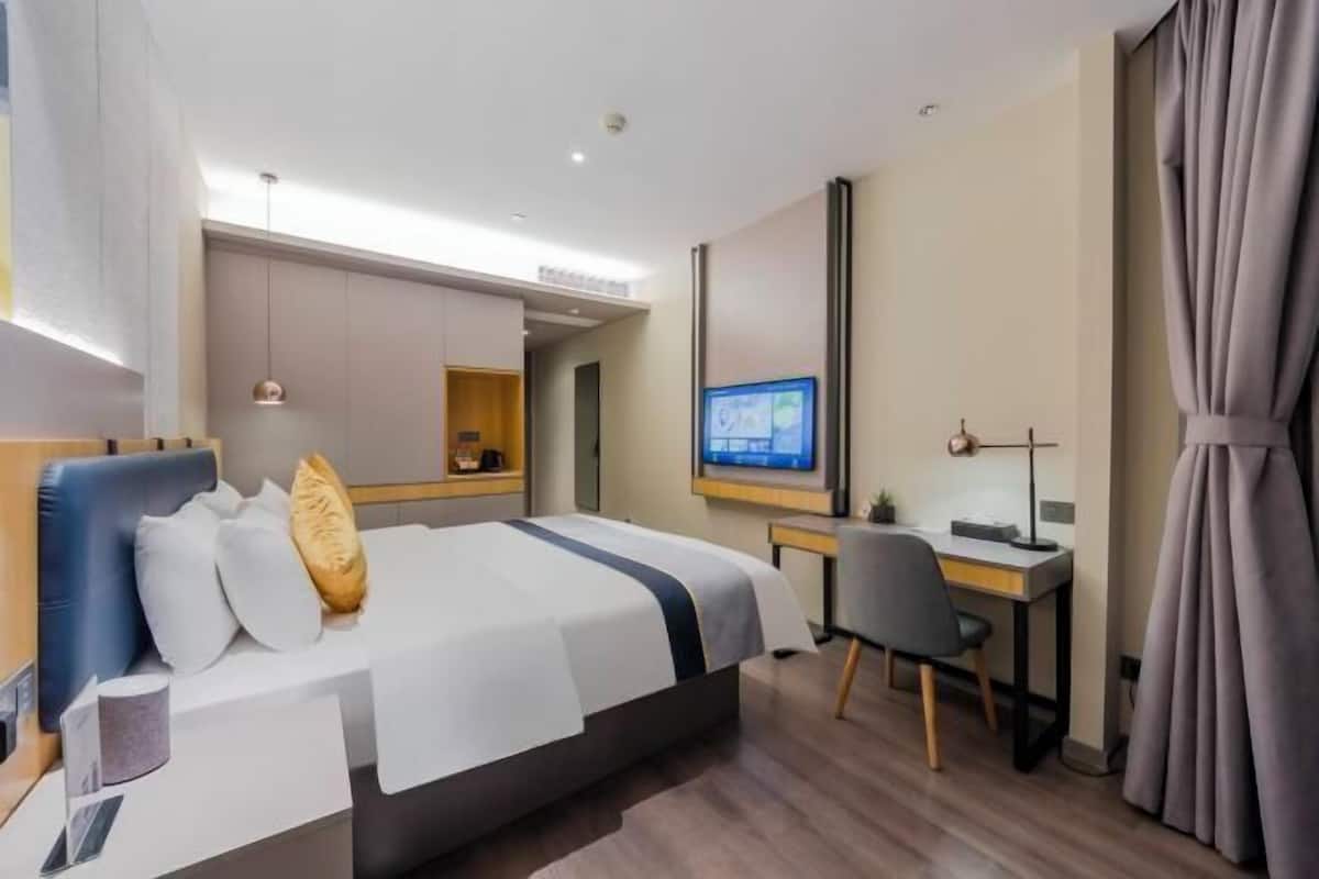 A modern hotel room with a large bed, a desk, and a television.