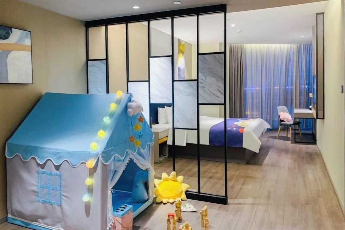 A bedroom with a bed, a desk, and a chair. There is a play tent and a sun-shaped toy on the floor.