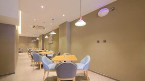 Un restaurante moderno con varias mesas y sillas, un largo pasillo e iluminación colgante.