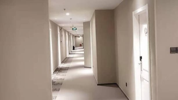 Un largo y estrecho pasillo de hotel con piso alfombrado y paredes blancas.
