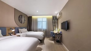 Habitación de hotel con dos camas, un escritorio, una silla, un televisor y una ventana con cortinas.