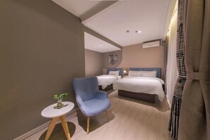 Et moderne hotelværelse med to senge, et lille rundt bord med en plante og en blå lænestol.
