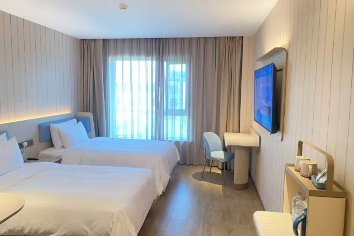 Quarto de hotel com duas camas, uma escrivaninha, uma cadeira, uma televisão e uma janela com cortinas.