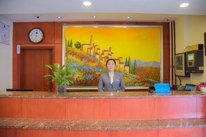 A hotel reception desk with a clock, a painting of a landscape, and a plant. - Hanting Hotel (jiuquan Changxing Electrical Equipm (Jiuquan)
