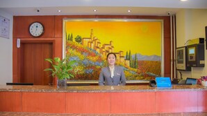 Un mostrador de recepción de hotel con un reloj, un cuadro de un paisaje y una planta.