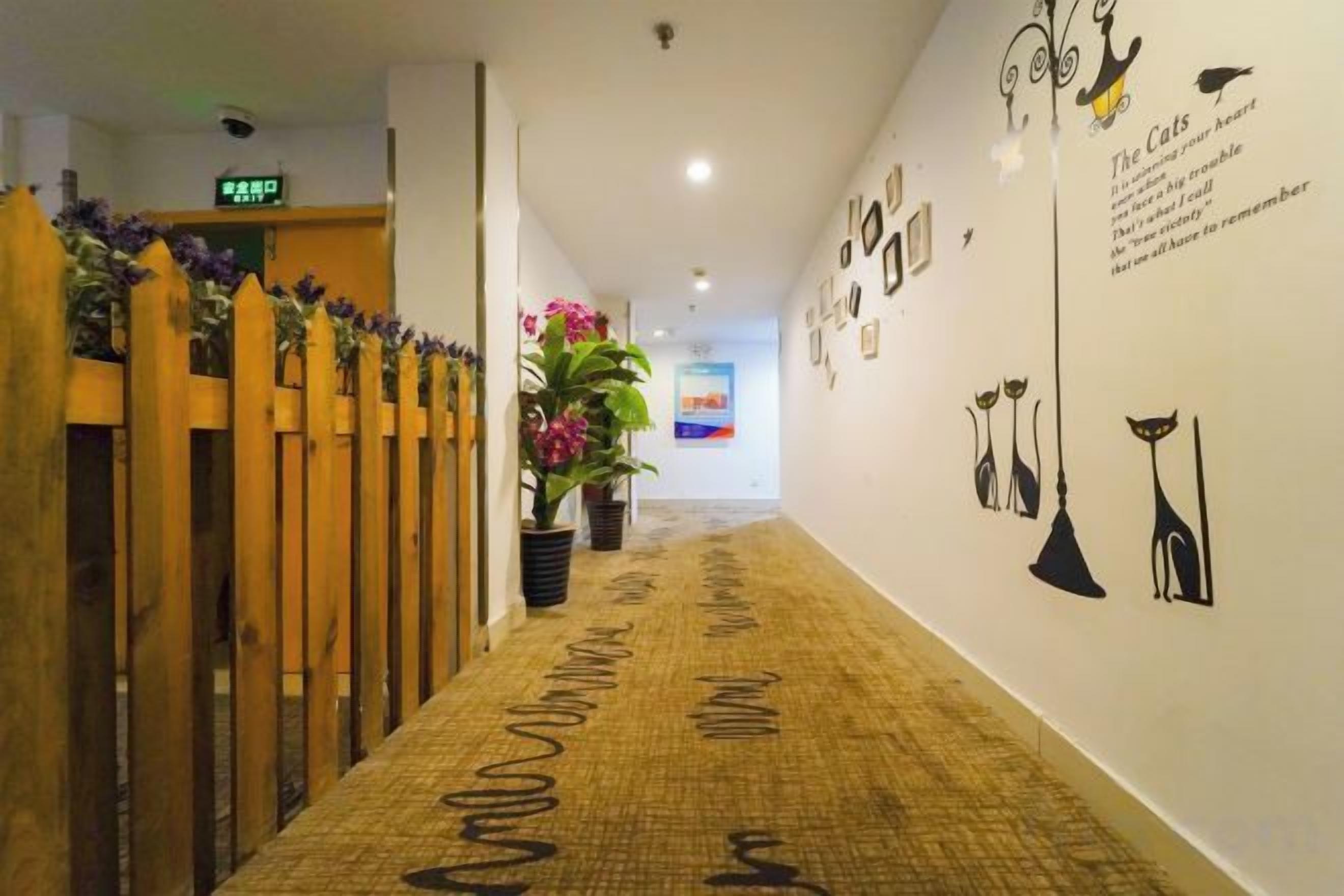 Un pasillo con alfombra estampada, valla de madera, plantas en macetas y adornos en la pared.