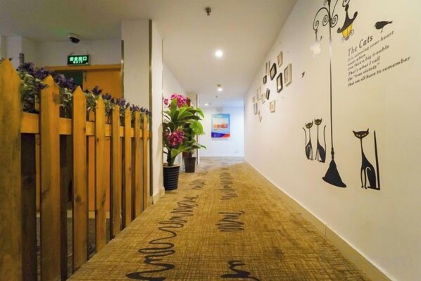 Un pasillo con alfombra estampada, valla de madera, plantas en macetas y adornos en la pared.