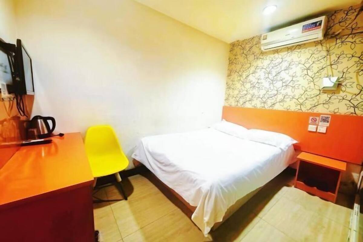 A small, single-bed room with a desk, a chair, and an air conditioning unit on the wall.