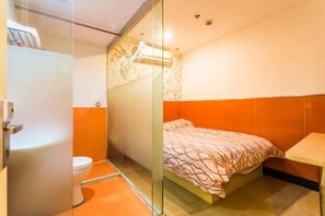 Una habitación pequeña y funcional con cama, inodoro y zona de ducha.