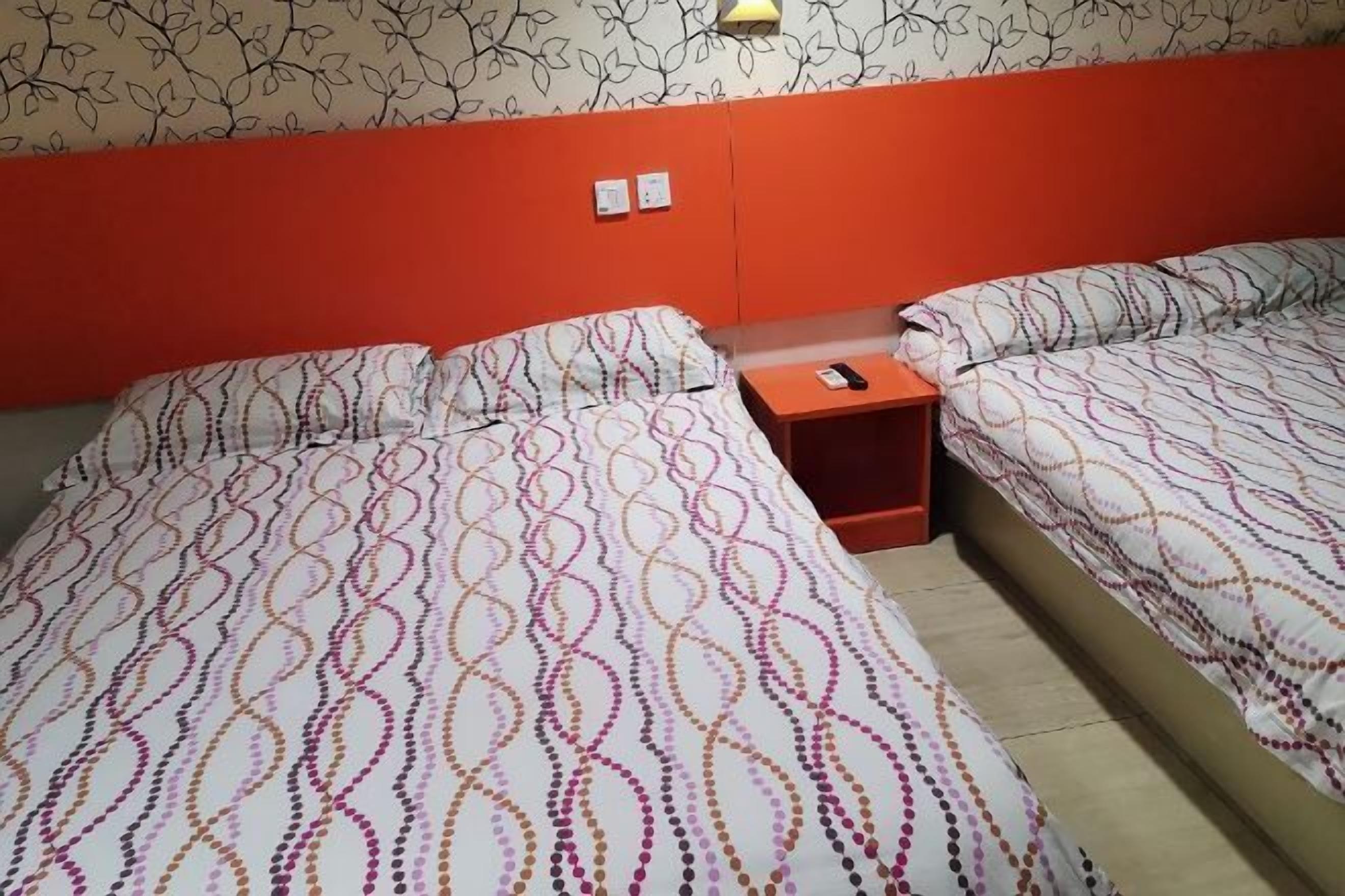 A hotel room with two beds, each with patterned bedding, a nightstand, and a wall-mounted lamp.