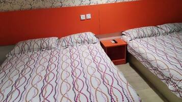 A hotel room with two beds, each with patterned bedding, a nightstand, and a wall-mounted lamp.