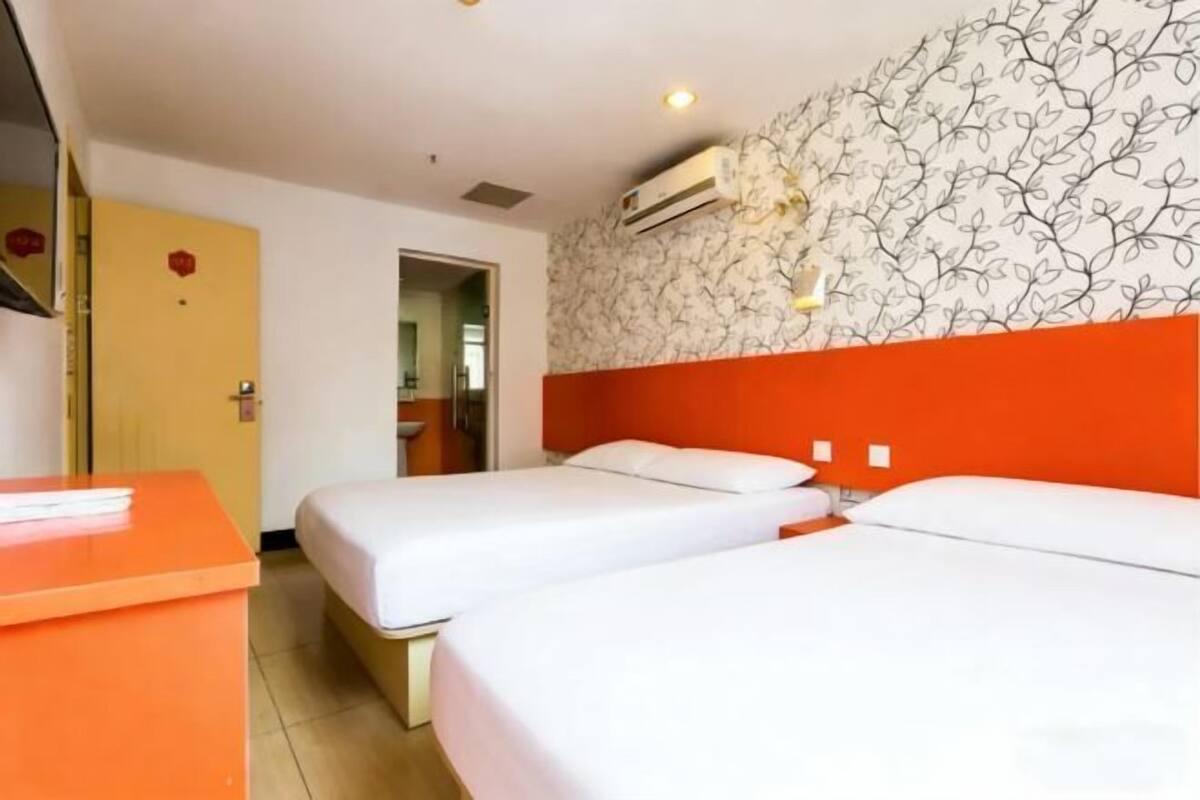 A hotel room with two beds, a desk, an air conditioning unit, and a patterned wall.