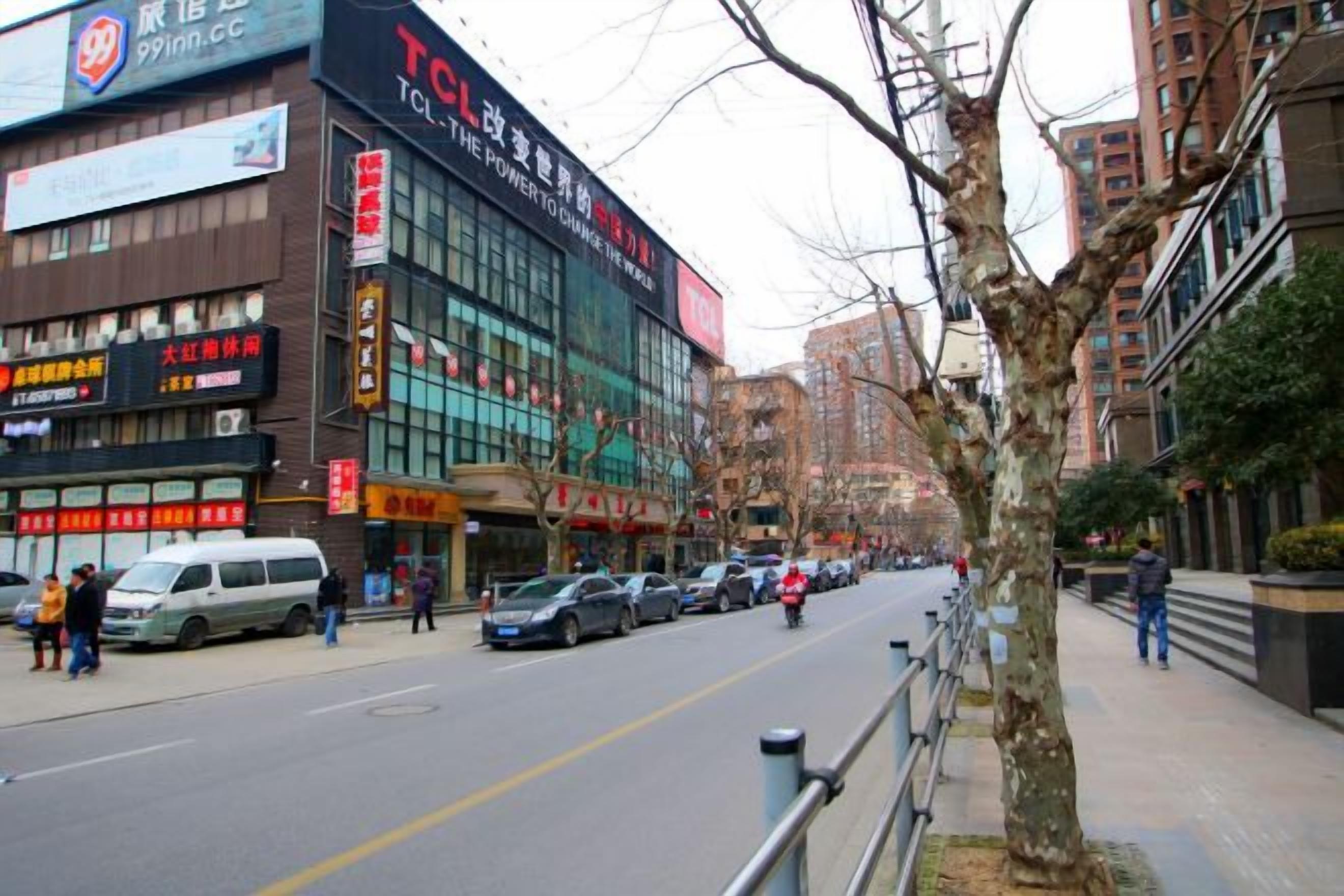 Vista de la calle con un edificio con la etiqueta 'TCL' y un árbol en primer plano.