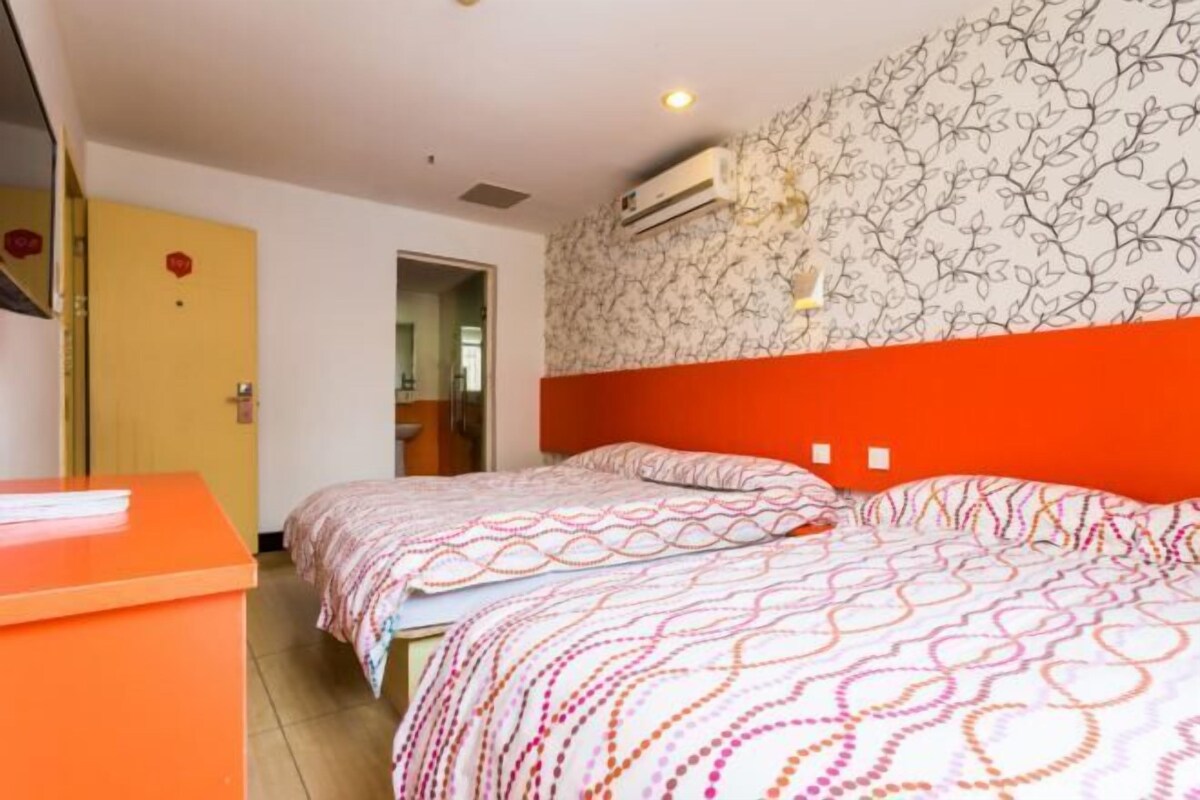 Habitación de hotel con dos camas, una pared decorada en rojo, un papel tapiz estampado y un pequeño escritorio.