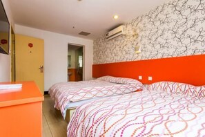 Habitación de hotel con dos camas, una pared decorada en rojo, un papel tapiz estampado y un pequeño escritorio.