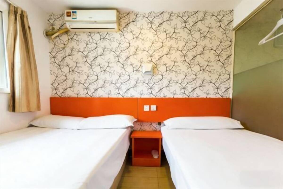 A room with two beds, an air conditioner, and a patterned wallpaper.