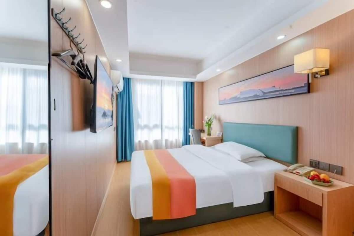 A hotel room with a bed, a nightstand, a painting, and a window with curtains.