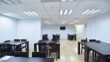 A conference room with multiple tables and chairs, a flat-screen TV mounted on the wall, and a tiled floor.