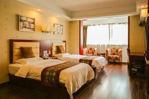 A hotel room with two beds, a sitting area with a chair, and a window with curtains.