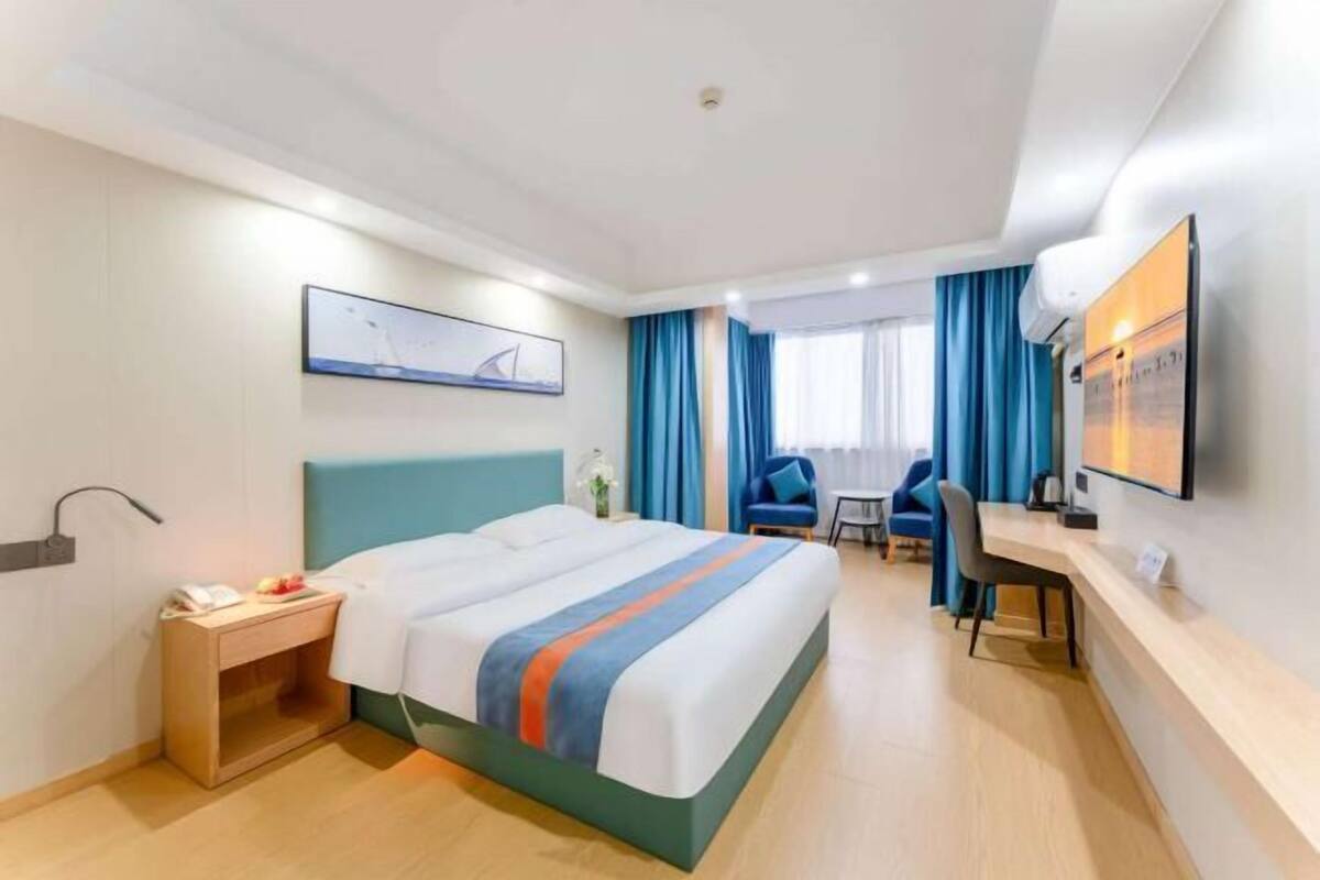 A hotel room with a bed, desk, chair, and artwork on the walls.