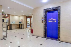Um saguão de hotel com balcão de recepção, elevador azul e piso em azulejos.