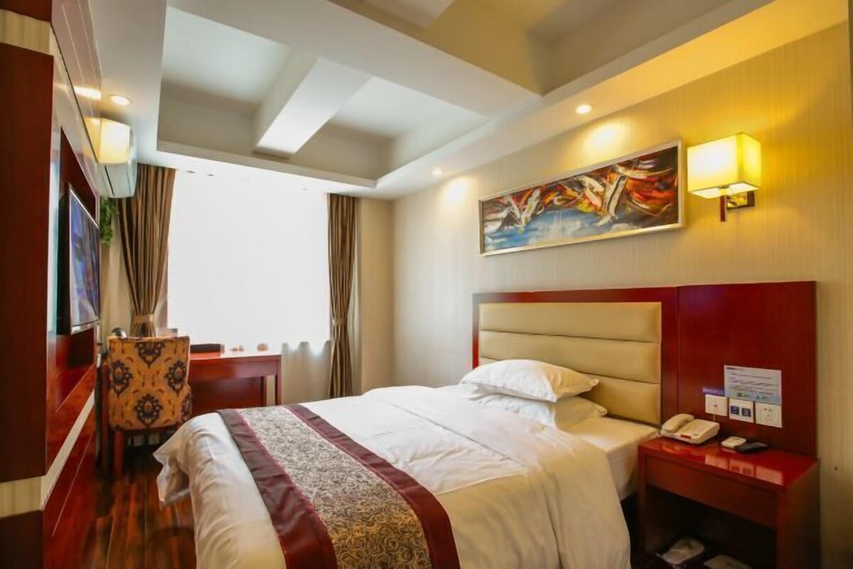 A hotel room with a large bed, a desk with a telephone, and a painting on the wall.
