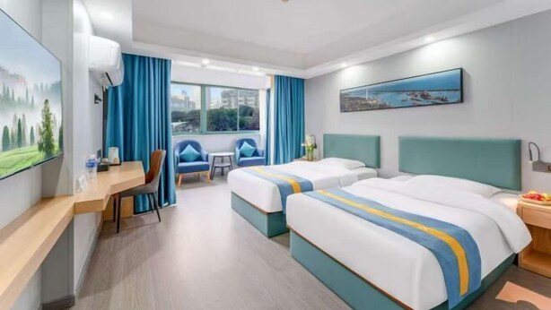 Habitació d'hotel amb dos llits, un escriptori, una cadira, una taula petita i una finestra amb cortines.