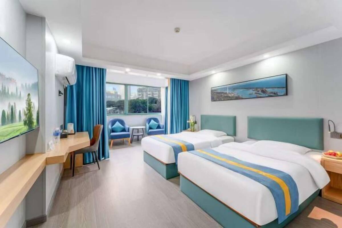 A hotel room with two beds, a desk, a chair, a small table, and a window with curtains.