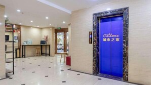Un vestíbul d'hotel amb un ascensor blau, una recepció i una zona de seients.