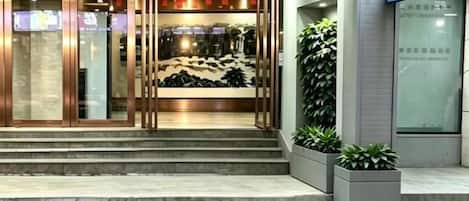 Entrada de hotel con puerta de vidrio, escalones que conducen a ella y un letrero sobre la puerta.