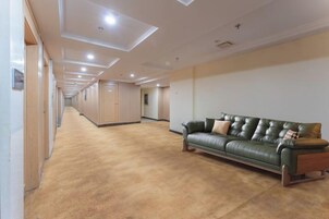 Un pasillo de hotel con un sofá de cuero verde, puertas de madera y suelo alfombrado.