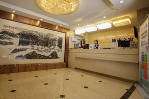 A hotel reception area with a large traditional painting, a reception desk, and a chandelier.