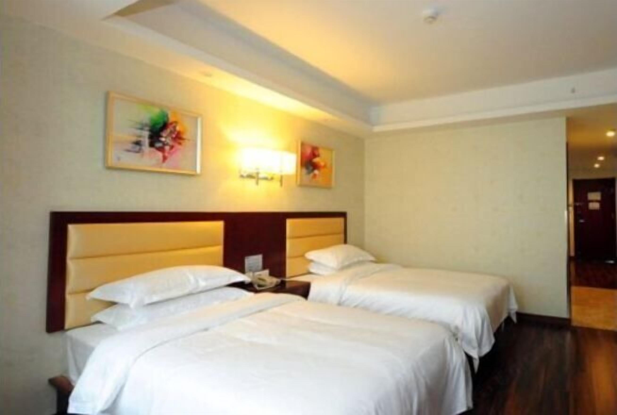A hotel room with two beds, a wooden headboard, a nightstand with a phone, and two wall-mounted lamps.