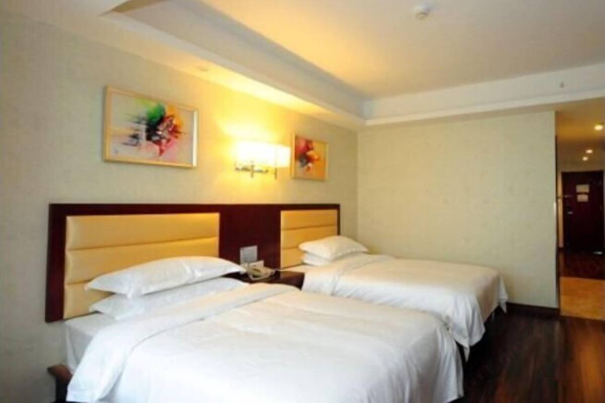 A hotel room with two beds, a wooden headboard, a nightstand with a phone, and two wall-mounted lamps.