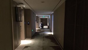 Un pasillo de hotel con piso alfombrado, una puerta a la izquierda y una rejilla de ventilación a la derecha.
