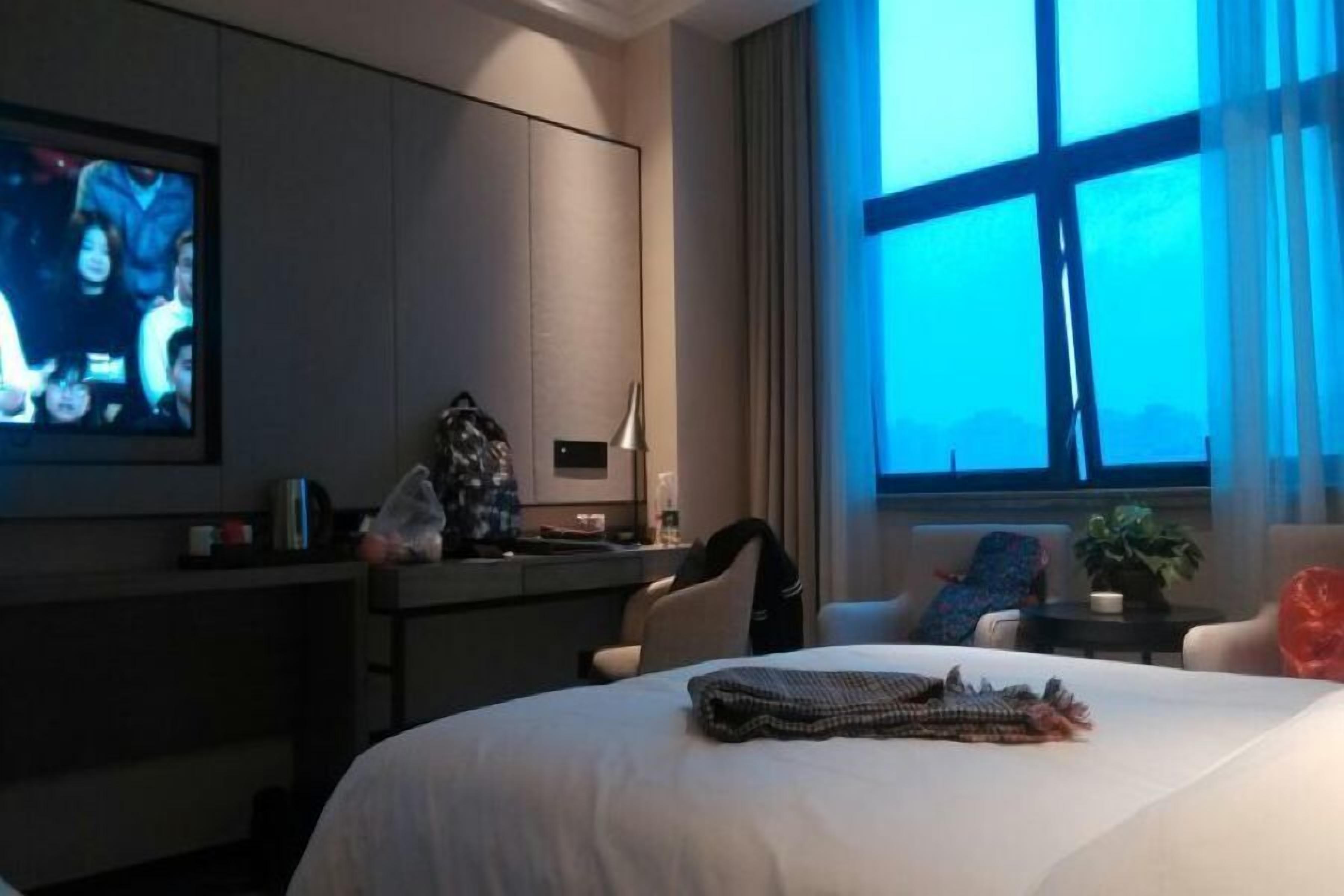 A hotel room with a bed, a desk, a television, and a window with curtains.