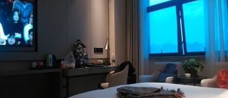A hotel room with a bed, a desk, a television, and a window with curtains.