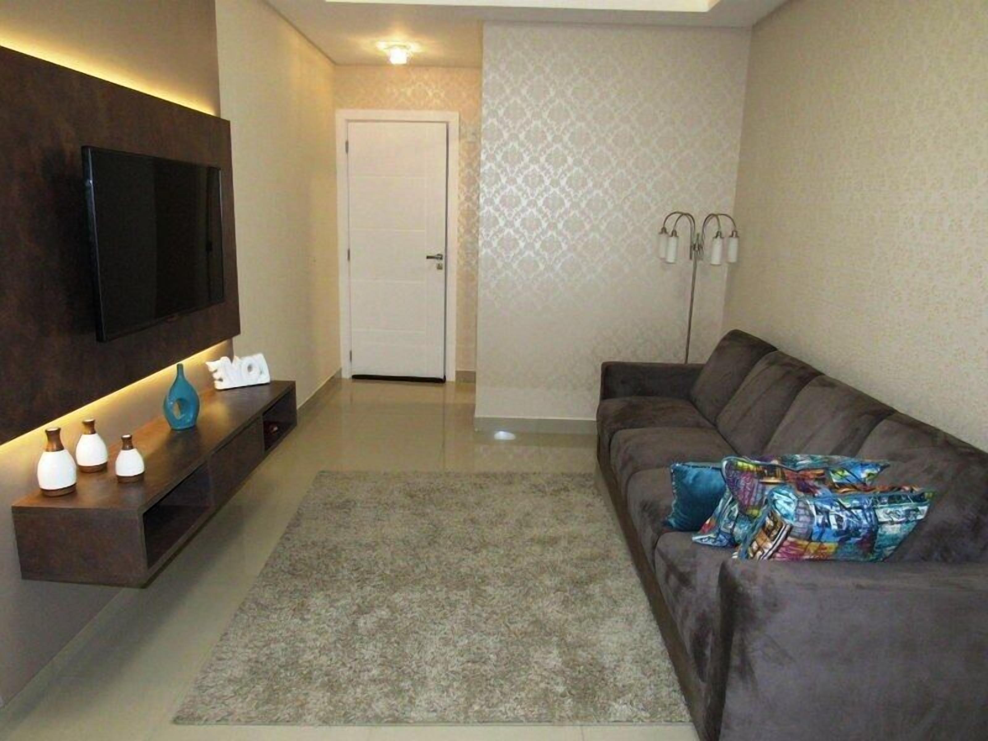 Una sala de estar moderna con un televisor de pantalla plana, un sofá marrón oscuro, un tapete estampado y una mesita de centro con jarrones decorativos.