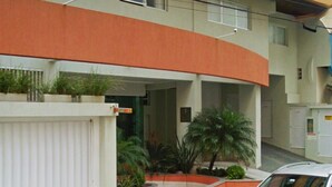 A modern building with a curved orange facade, a covered entrance, and a parking area with a white car. - Apartamento a 200m do Mar BCHost 17 (Itapema)