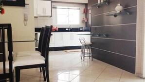 A modern kitchen with white cabinets, a black countertop, and a glass dining table with two chairs. - Apartamento a 200m do Mar BCHost 17 (Itapema)