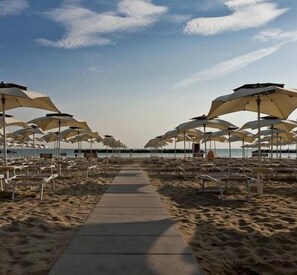 A beach with rows of umbrellas and chairs along a central walkway. - Hotel Plaza (Pesaro)