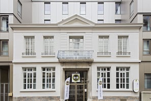 La façade d’un hôtel présente un design symétrique, de grandes fenêtres et une entrée centrale.
