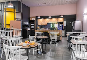 Un café avec des chaises et des tables blanches, un coin bar et un réfrigérateur portant l’inscription « Vert citron ».