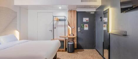Una habitación de hotel con una cama, un escritorio, un espejo y una puerta.