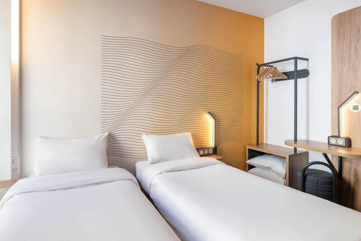 Een hotelkamer met twee bedden, een nachtkastje, een lamp en een kapstok aan de muur.