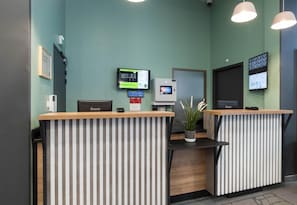 A reception area with two counters, a digital display, a potted plant, and a door. - B&B HOTEL LYON Centre Perrache (Lyon)